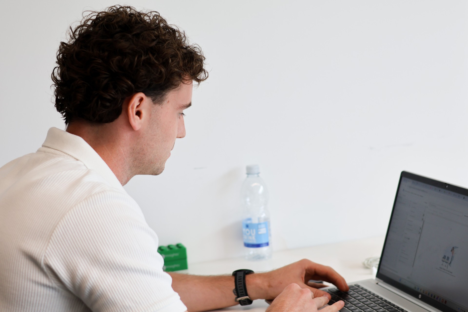 Man working at a laptop at a desk, with a water bottle beside him.