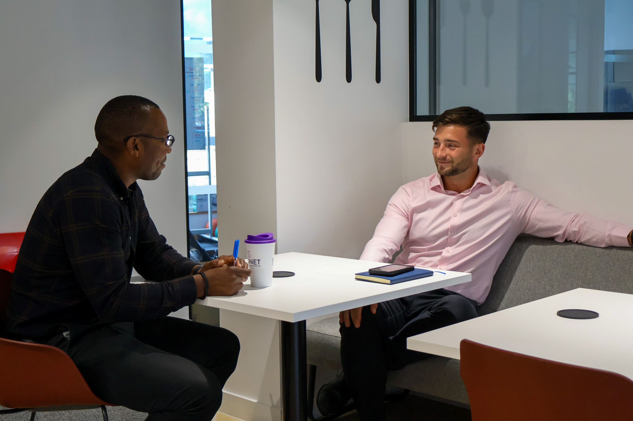 A Signet Resources team member shares insights from a notebook with a smiling colleague, enhancing their recruitment approach.