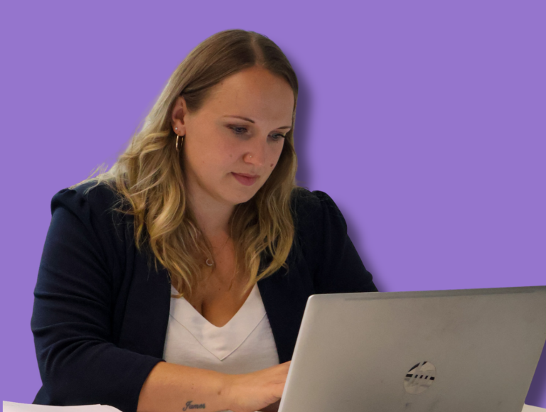 Signet Resources employee reviews recruitment data on a laptop while taking notes, highlighting a multitasking work environment.