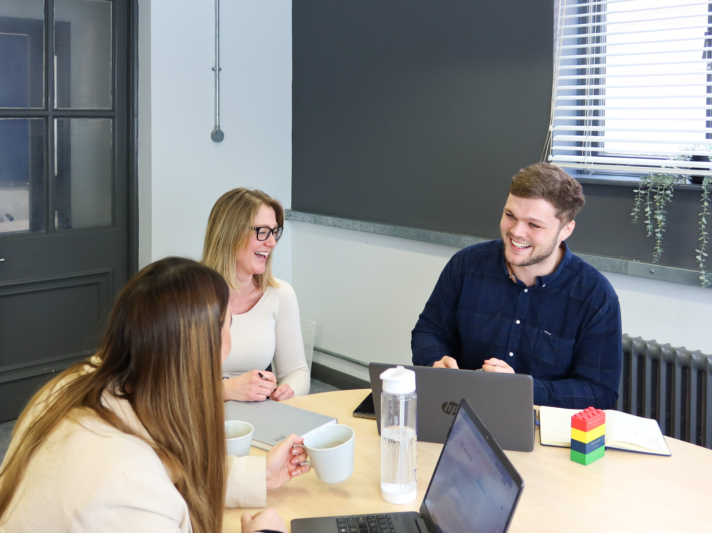 Three colleagues from Signet Recruitment and Retention enjoying a light-hearted moment during a recruitment strategy meeting.