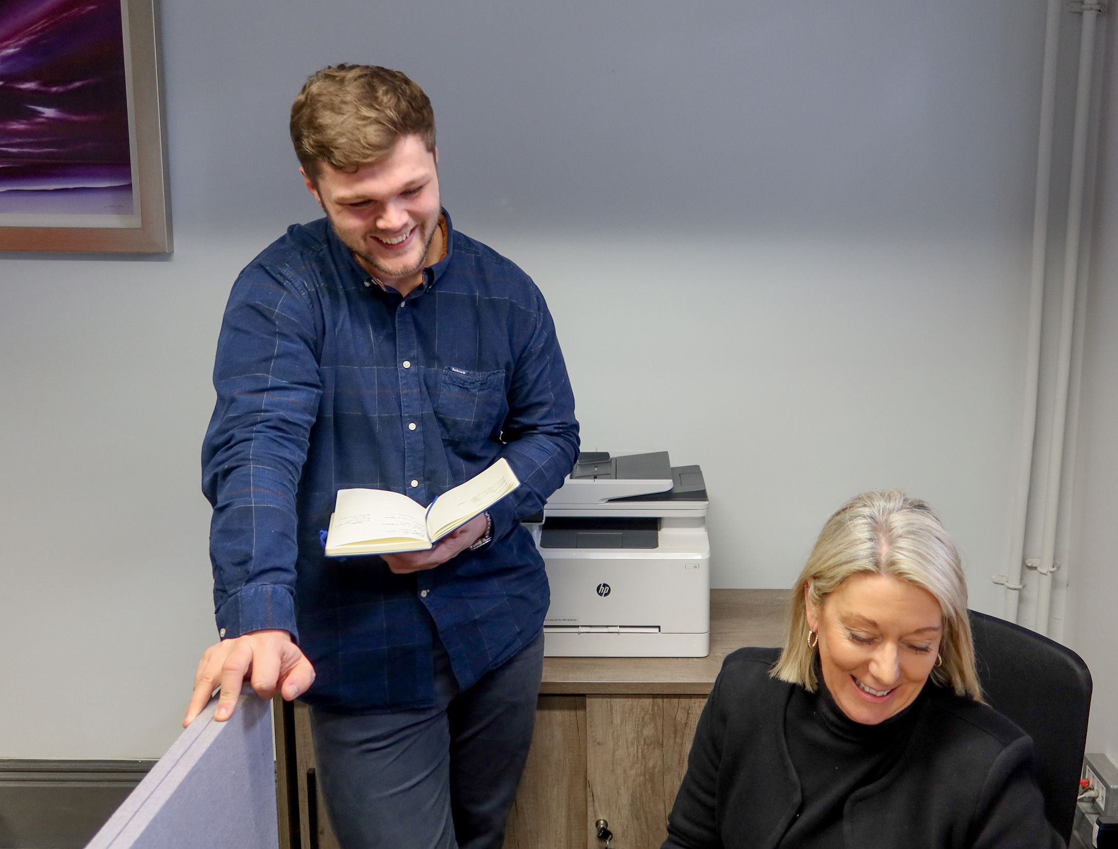 A Signet Resources team member shares insights from a notebook with a smiling colleague, enhancing their recruitment approach.