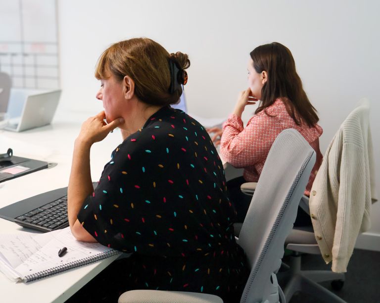 Signet Resources employee reviews recruitment data on a laptop while taking notes, highlighting a multitasking work environment.